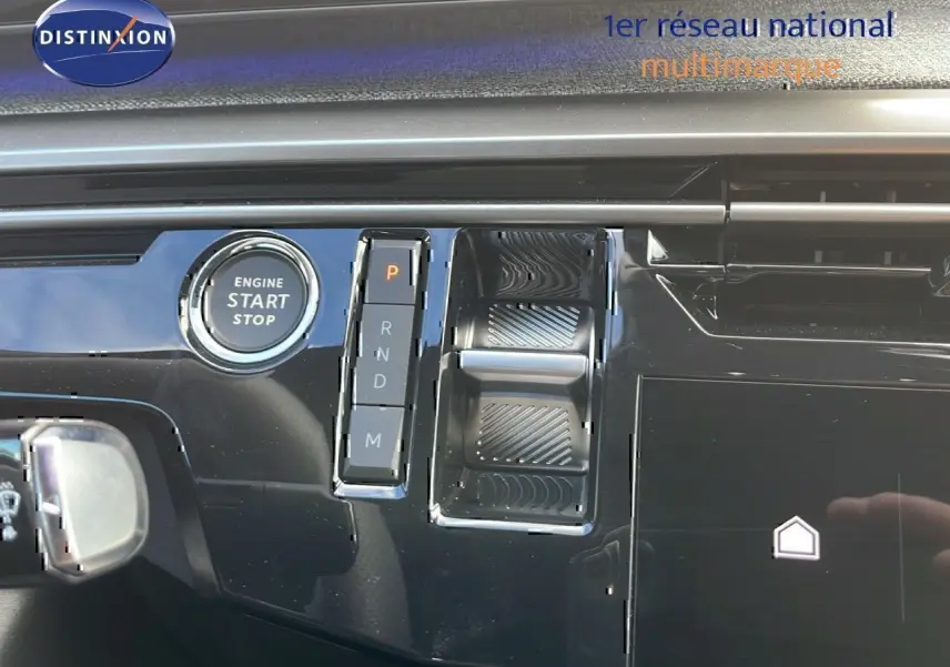 Gros plan sur la console centrale noire brillante du Peugeot 3008 hybride 2025 avec bouton start/stop et sélecteur de boîte automatique.