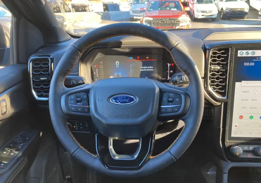 Vue intérieure centrée sur le volant en cuir avec surpiqûres marron du Ford Ranger 2025 Bleu Lightning, tableau de bord numérique visible.