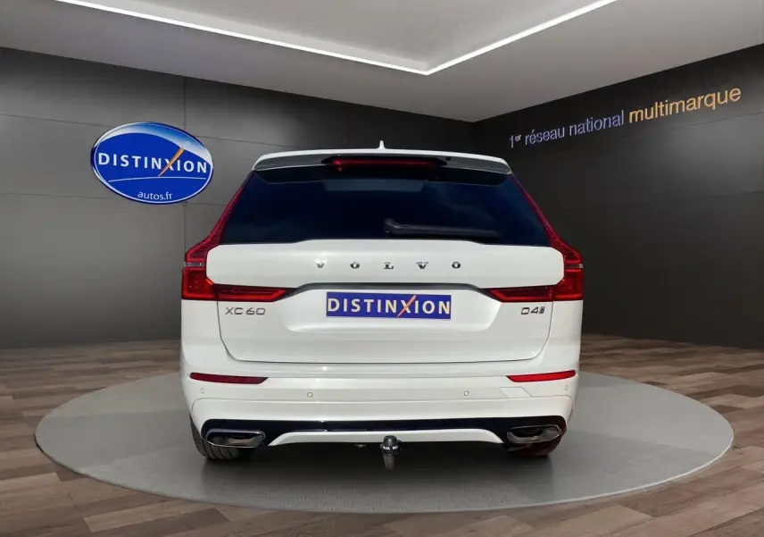 Vue arrière d'un Volvo XC60 D4 blanc avec attelage et feux arrière LED dans un showroom.
