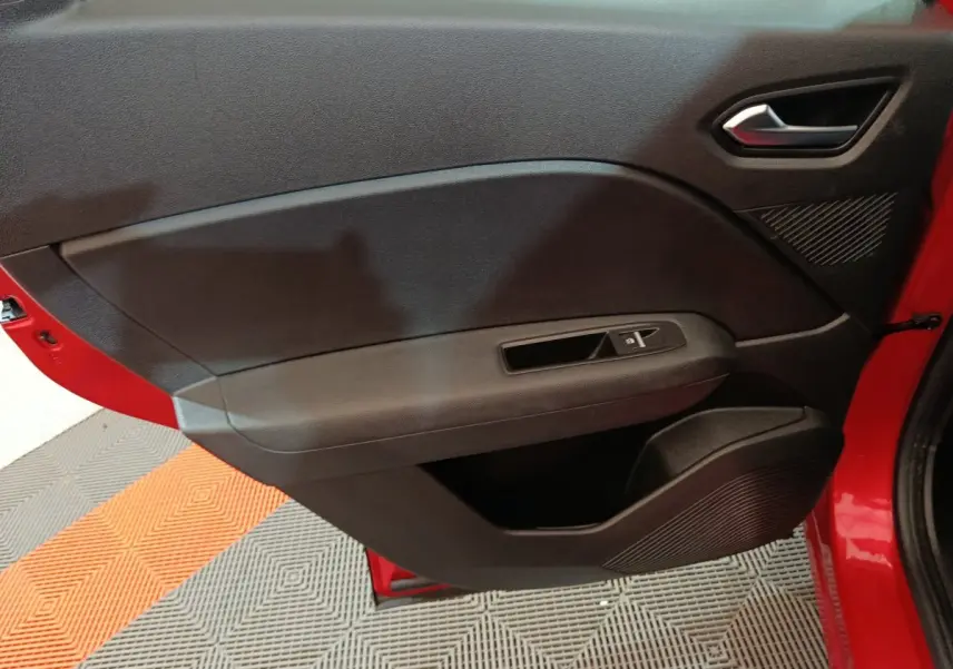 Vue rapprochée de la porte avant gauche rouge du Renault Captur 2024 avec commandes de vitre et poignée intégrée.