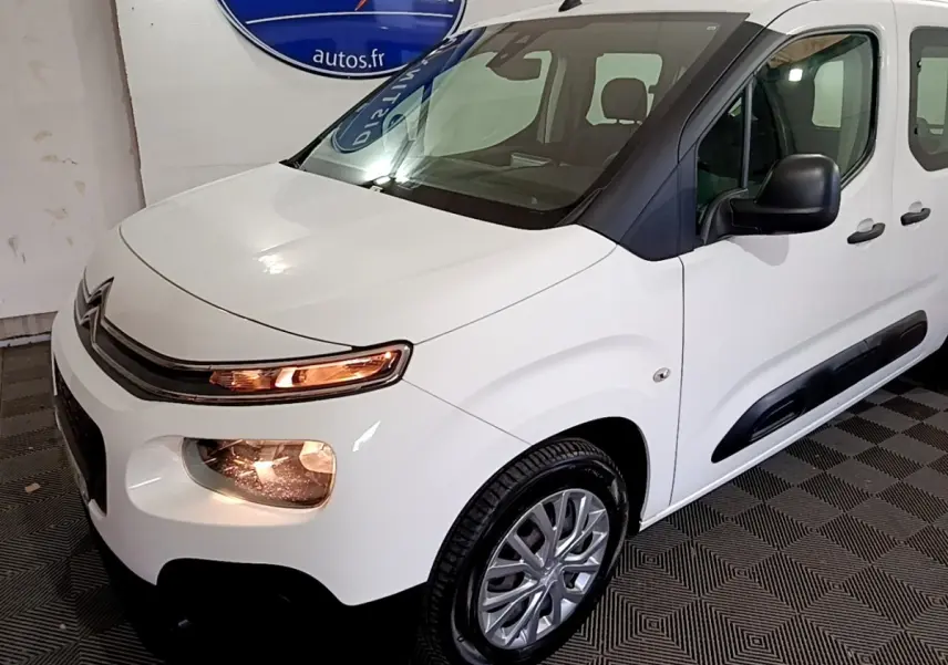 Vue 3/4 avant droit d'un Citroën Berlingo blanc 2019 avec phares allumés et protections latérales noires.