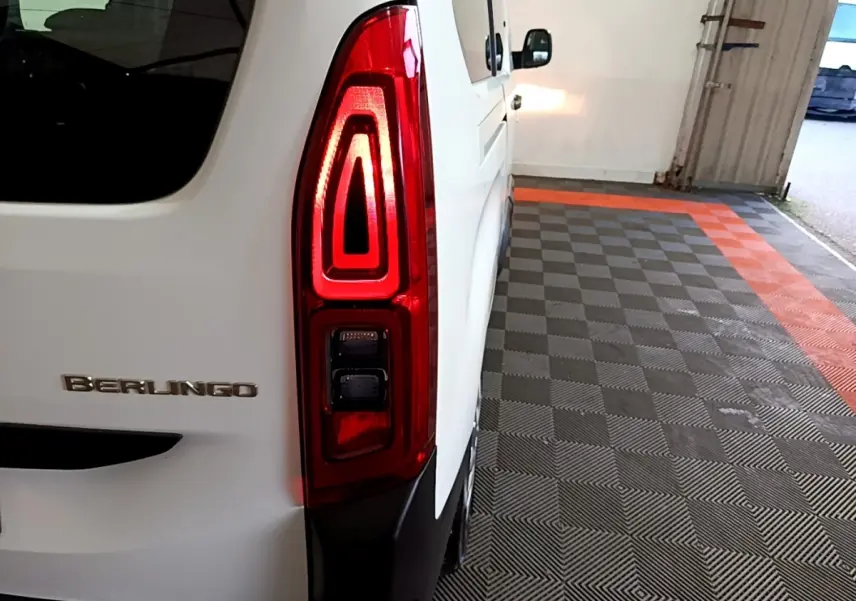 Vue arrière côté gauche d'un Citroën Berlingo blanc XL avec feu arrière allumé dans un garage.