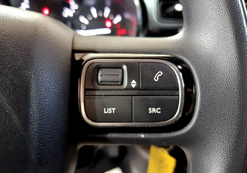 Gros plan sur les commandes multifonctions noires du volant d’une Citroën C3 2017, avec boutons LIST et SRC visibles.