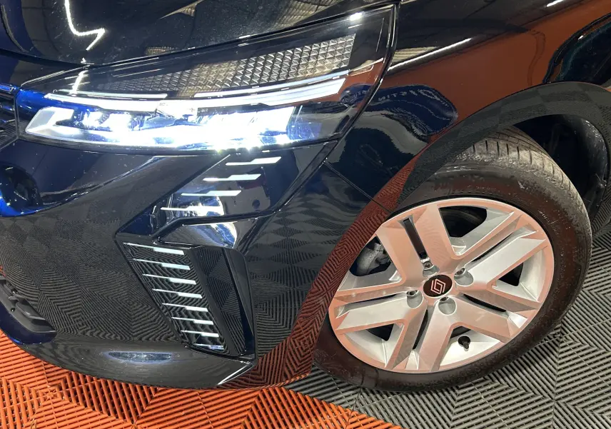 Gros plan sur l’avant droit noir brillant de la Renault Clio V avec phare LED allumé et jante alliage distinctive.