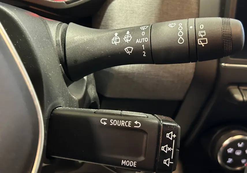 Gros plan sur les commandes de lève-glace et essuie-glace à gauche du volant d'une Renault Clio V noire.