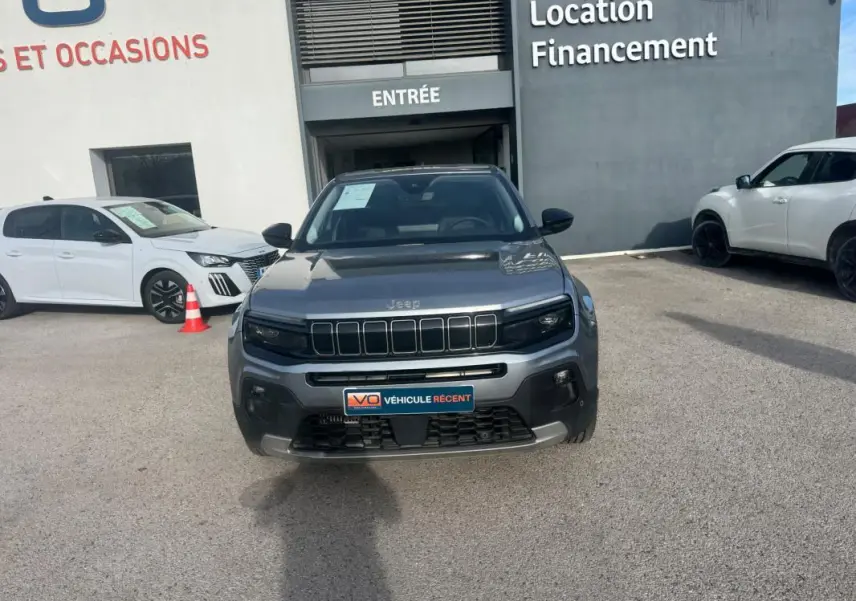 Vue avant d'un Jeep Avenger gris 2025 garé devant un bâtiment avec plaque V.O. Véhicule récent.