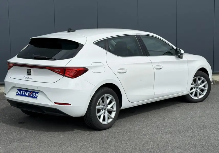 Vue 3/4 arrière droite d'une SEAT Leon blanche avec vitres arrière surteintées et jantes alliage 16 pouces.