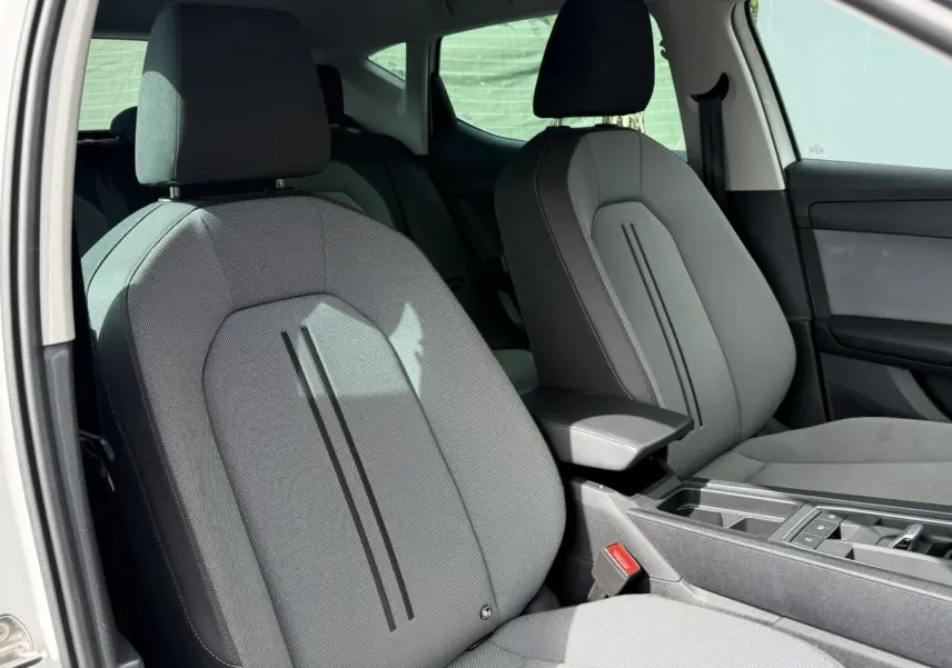 Vue intérieure côté avant gauche des sièges tissu gris d’une SEAT LEON blanche avec accoudoir central et console.