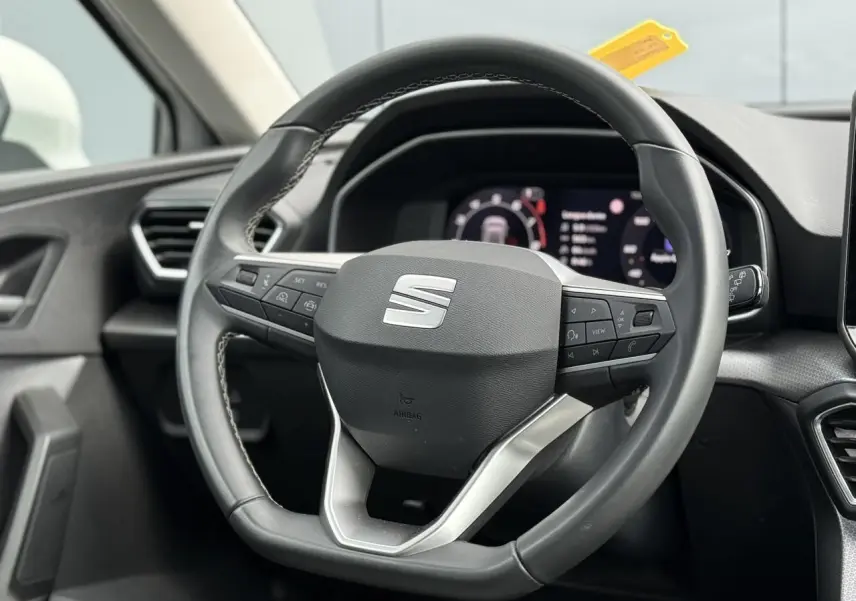 Vue rapprochée du volant cuir multifonction de la SEAT LEON 2025, avec tableau de bord numérique en arrière-plan.