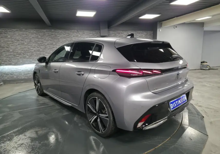 Vue 3/4 arrière gauche d'une Peugeot 308 gris métallisé 2024 avec feux arrière LED et jantes alliage 18 pouces.