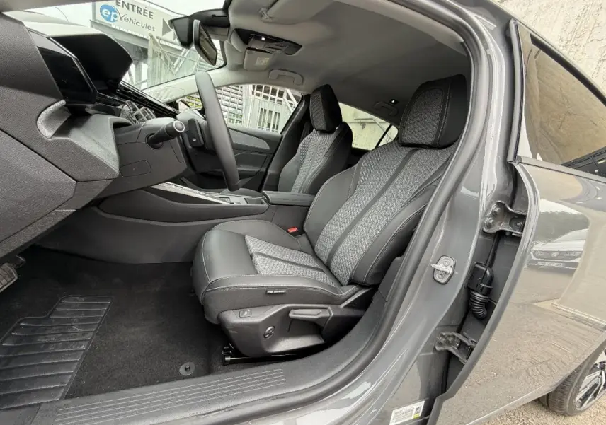 Vue intérieure côté conducteur de la Peugeot 308 gris sellenium, mettant en valeur les sièges en tissu et cuir avec surpiqûres.