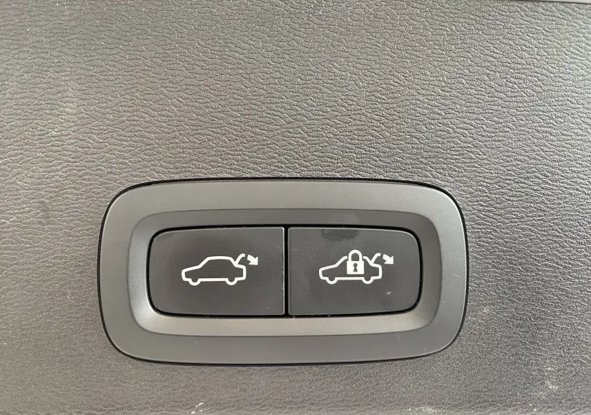 Boutons de commande du coffre avec ouverture et verrouillage sur fond noir texturé, intérieur d'un Volvo XC40 argenté.
