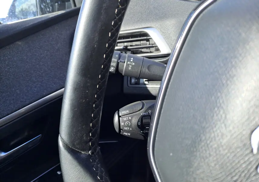 Gros plan sur le volant noir et les commandes de régulateur de vitesse du Peugeot 3008 Metallic Cooper, intérieur gris.