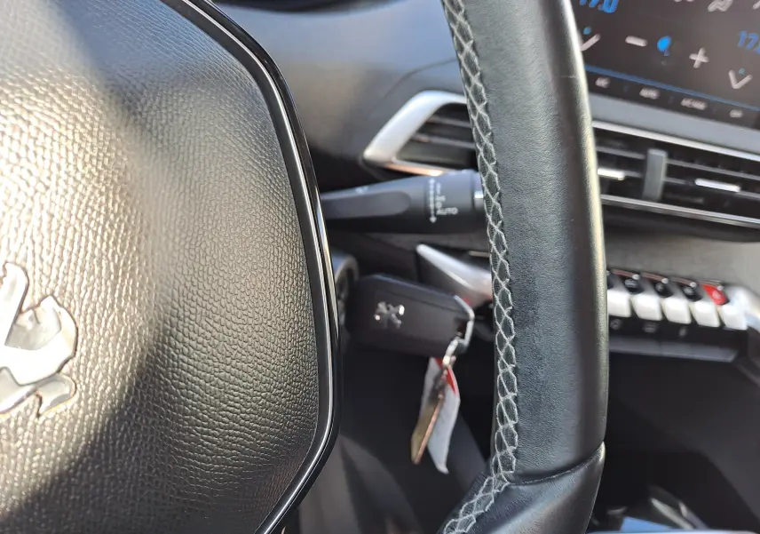 Gros plan sur le volant en cuir noir avec logo Peugeot et tableau de bord numérique en arrière-plan du 3008 Metallic Cooper.