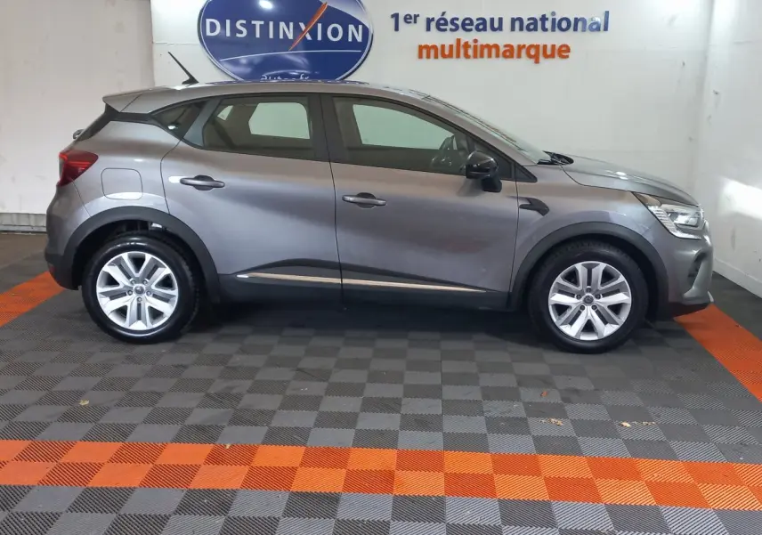 Profil droit d'un Renault Captur Business TCe 100 gris clair stationné en intérieur sur un sol damier gris et orange.