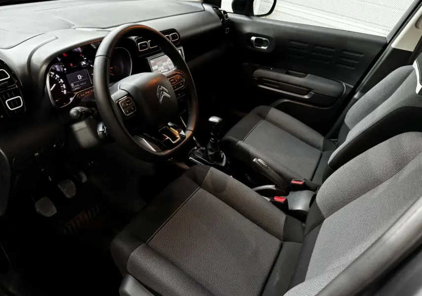 Intérieur avant droit du Citroën C3 Aircross 2024, sièges tissu gris, volant cuir multifonctions et tableau de bord noir.