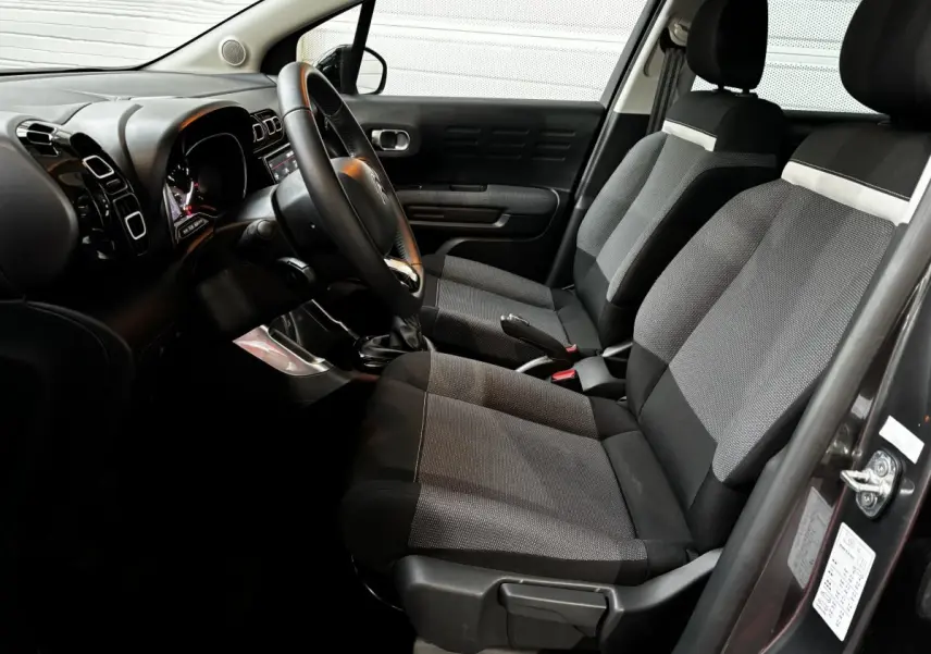 Vue intérieure côté conducteur de la Citroën C3 Aircross gris foncé, sièges tissu bicolore et tableau de bord moderne.