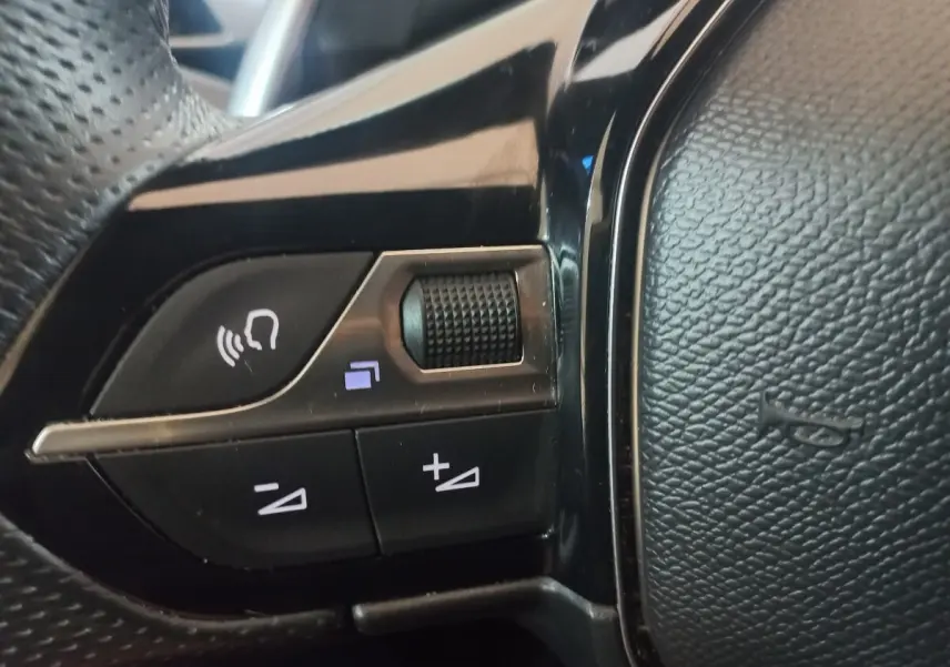 Gros plan sur les commandes vocales et volume du volant cuir noir du Peugeot 3008 PureTech gris clair, version 2022.