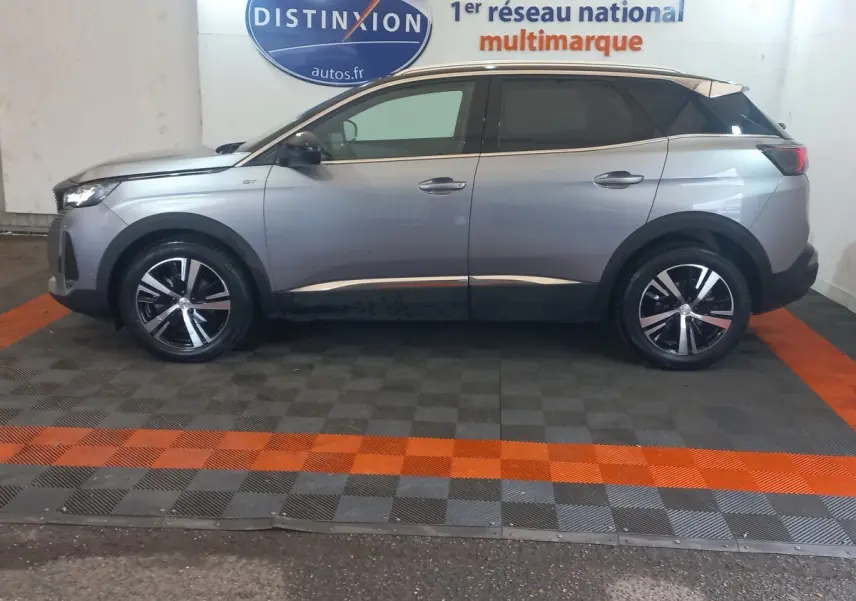 Vue latérale droite d'un Peugeot 3008 gris clair 2022 avec toit noir et jantes alliage bicolores, en intérieur showroom.