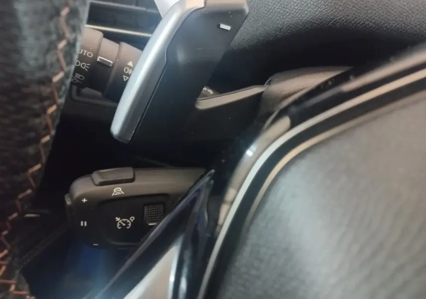 Gros plan sur la commande de régulateur de vitesse et palettes au volant du Peugeot 3008 gris clair, intérieur noir.