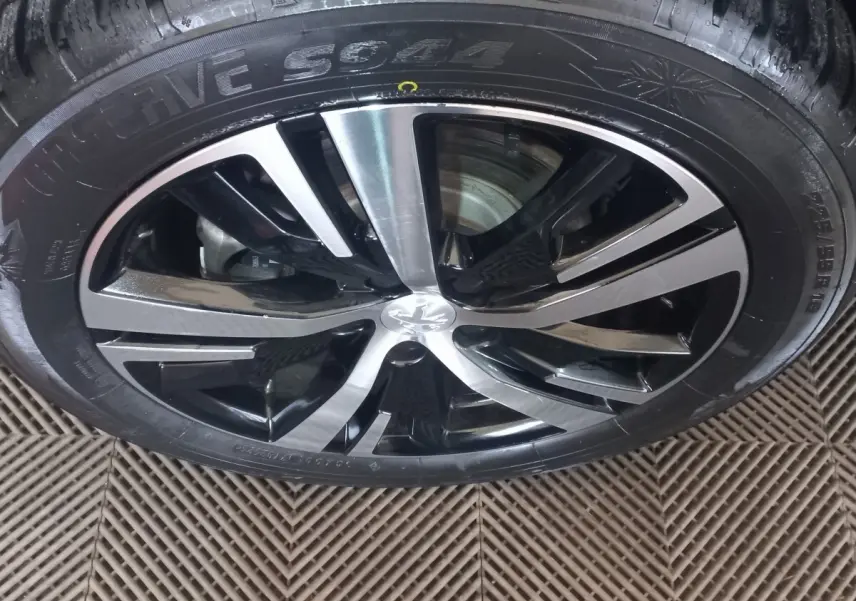 Gros plan sur la jante alliage bi-ton noir et argent avec logo Peugeot, montée sur pneu hiver sur sol texturé.