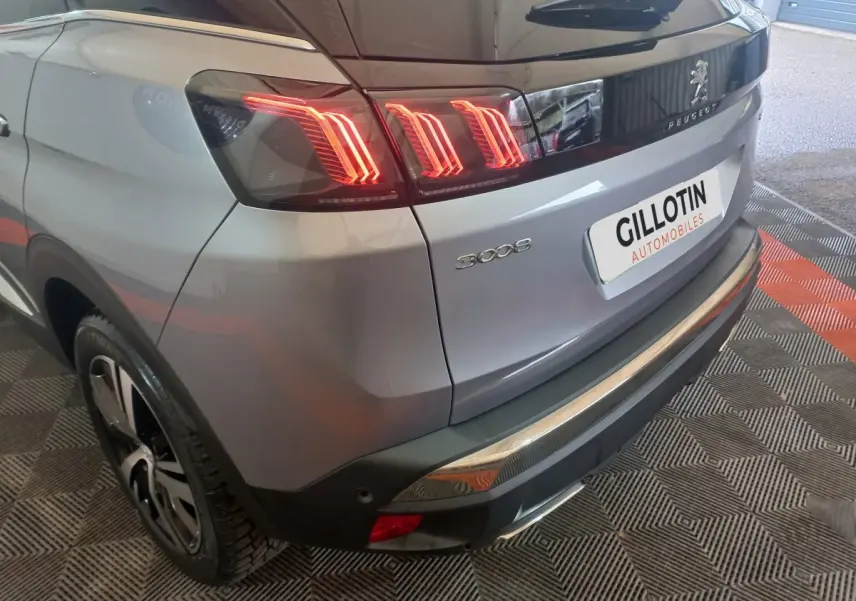 Vue 3/4 arrière droite d’un Peugeot 3008 gris clair avec feux arrière LED allumés et logo visible sur le hayon.