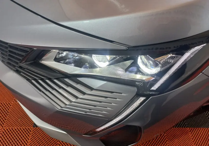 Gros plan sur le phare avant droit d’un Peugeot 3008 gris clair 2022 avec signature lumineuse LED distinctive.