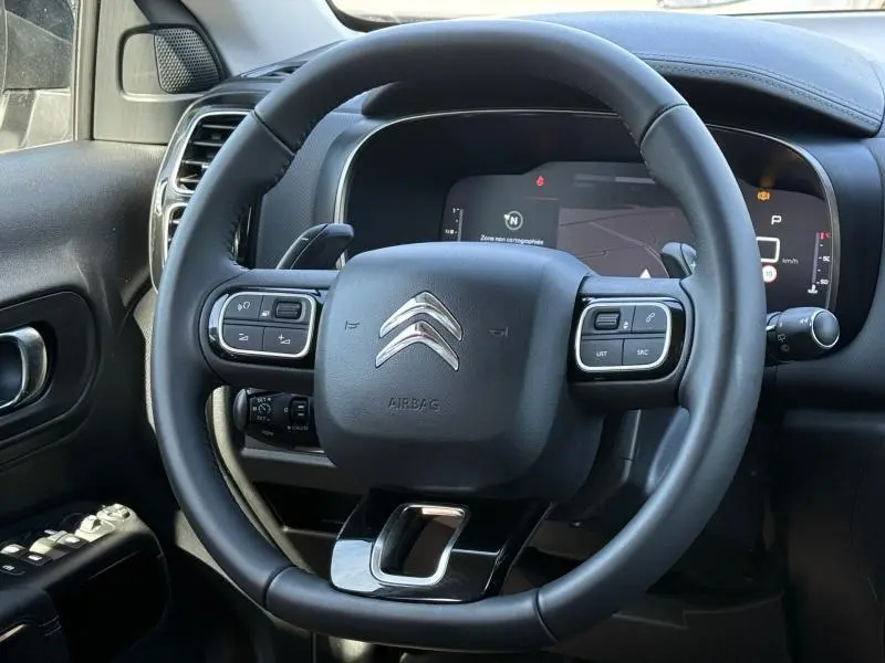 Vue rapprochée du volant noir du Citroën C5 Aircross 2025, avec commandes intégrées et tableau de bord numérique en arrière-plan.