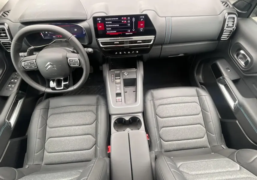 Vue intérieure avant du Citroën C5 Aircross 2025, sièges gris et noir avec tableau de bord numérique et écran tactile central.