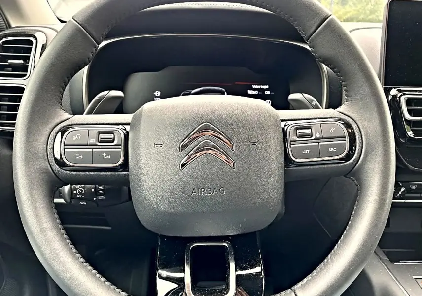 Vue rapprochée du volant noir du Citroën C5 Aircross 2025 avec commandes multifonctions et logo chromé central.