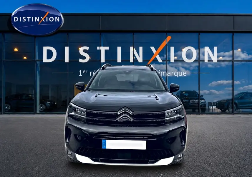 Vue frontale d’un Citroën C5 Aircross noir 2025, avec calandre distinctive et phares LED, devant une vitrine bleue.