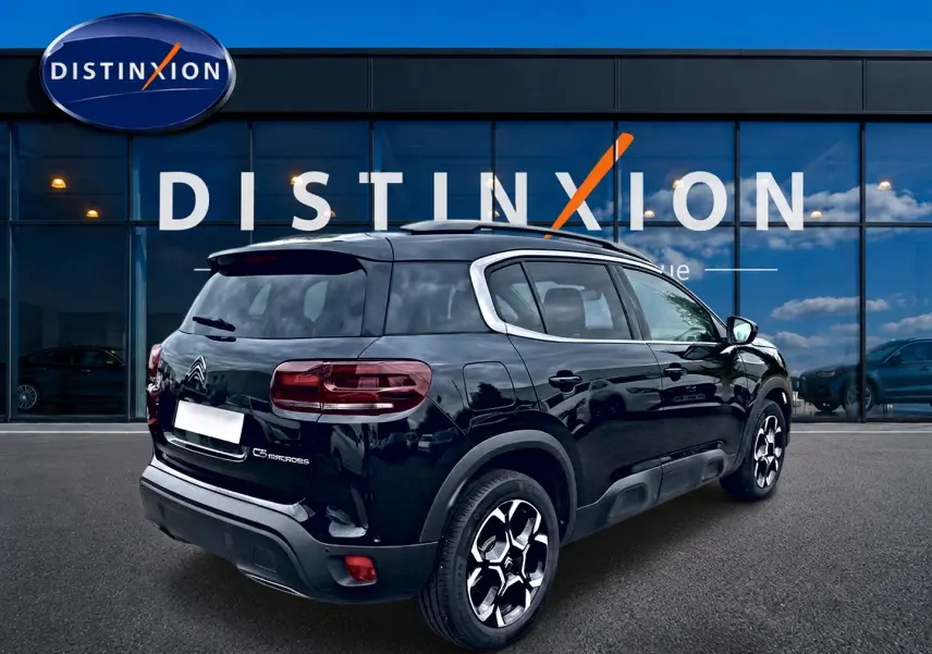 Vue 3/4 arrière droite d’un Citroën C5 Aircross noir avec jantes alu et vitres teintées devant un showroom Distinxion.