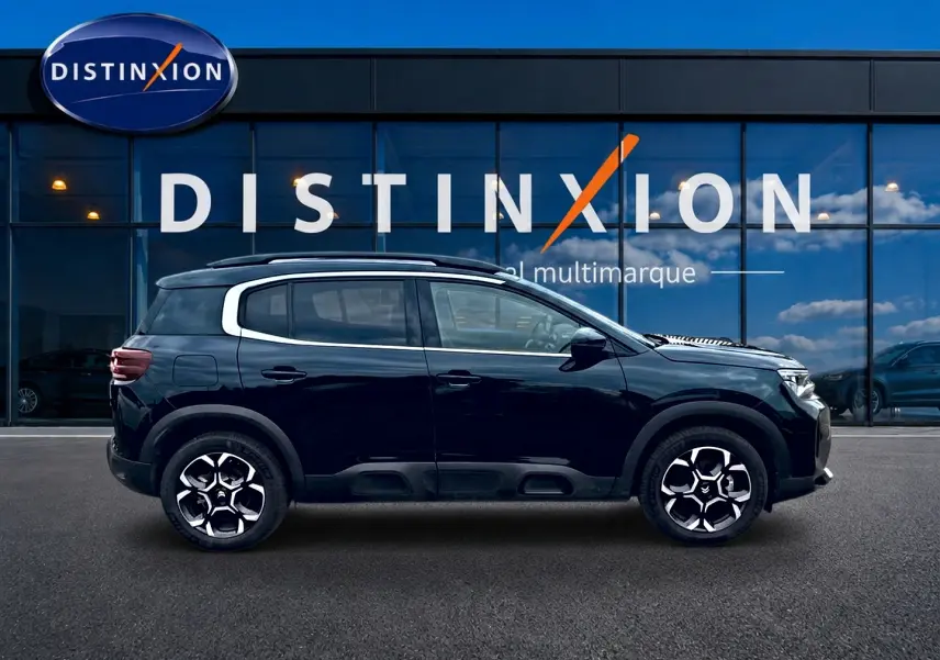 Profil droit d'un Citroën C5 Aircross noir 2025 avec jantes alu et barres de toit, devant une vitrine Distinxion.
