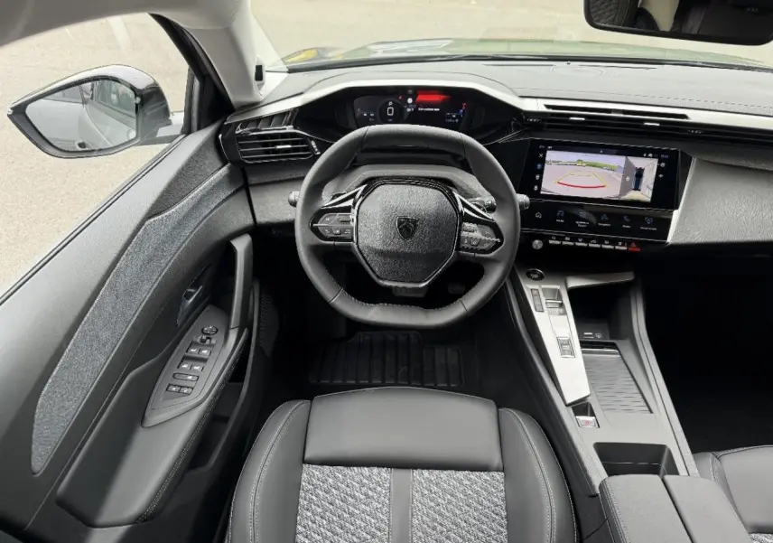 Vue intérieure avant de la Peugeot 308 2026, tableau de bord moderne avec écran tactile et volant compact noir.