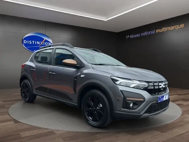 Vue 3/4 avant droite d'une Dacia Sandero Stepway TCE 110 Extreme Plus gris urban avec jantes noires et barres de toit noires.