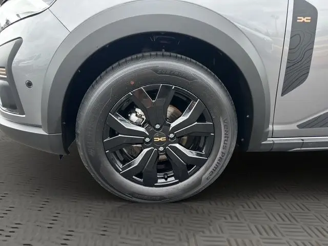 Gros plan sur la jante alu noire 16'' côté avant gauche d'une Dacia Sandero Stepway gris urban avec logo DC sur la carrosserie