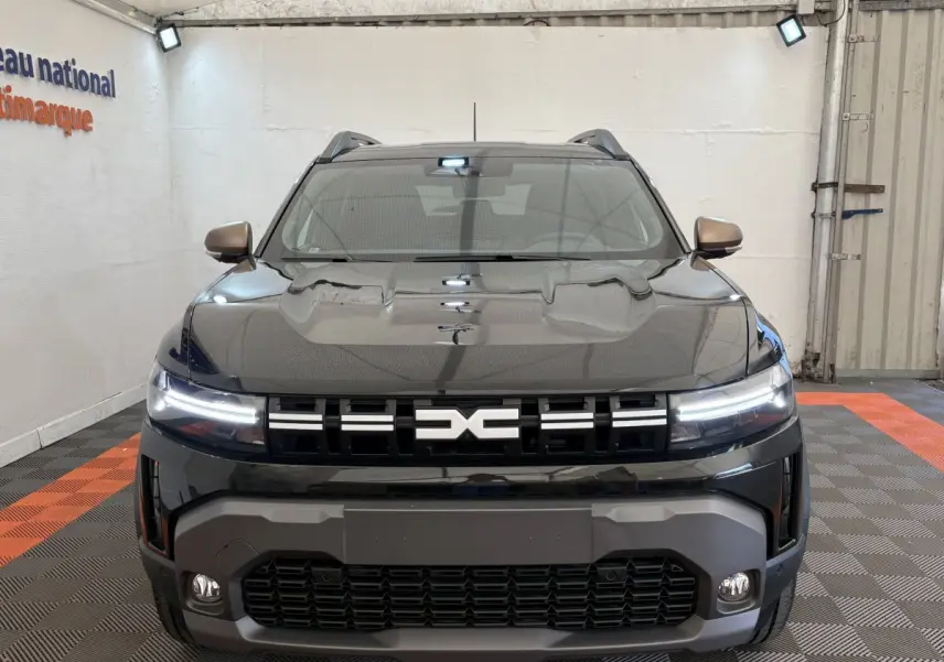 Vue frontale d'un Dacia Duster noir 2025 avec phares LED allumés et calandre marquée du logo DACIA.