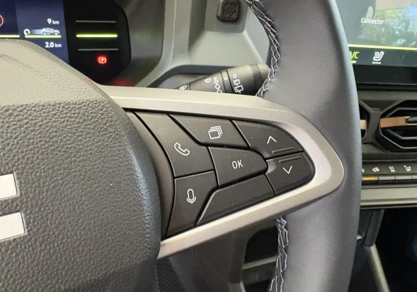 Gros plan sur le côté droit du volant cuir synthétique du Dacia Duster noir 2025 avec commandes multifonctions et tableau de bord numérique.