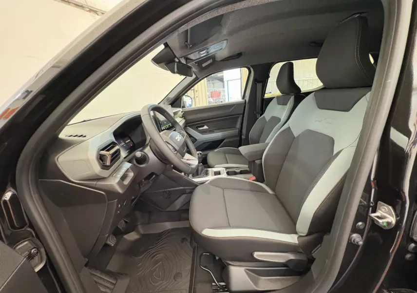 Intérieur avant droit du Dacia Duster noir 2025, sièges bicolores gris et noir avec volant multifonctions en vue rapprochée.