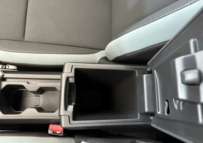 Gros plan sur la console centrale ouverte du Dacia Duster noir 2025, montrant le rangement intérieur et les surpiqûres orange des sièges.