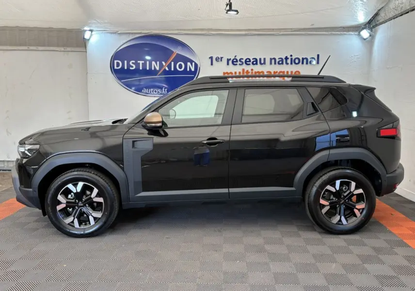 Profil droit du Dacia Duster noir 2025 avec jantes bicolores et rétroviseurs couleur bronze en intérieur showroom.