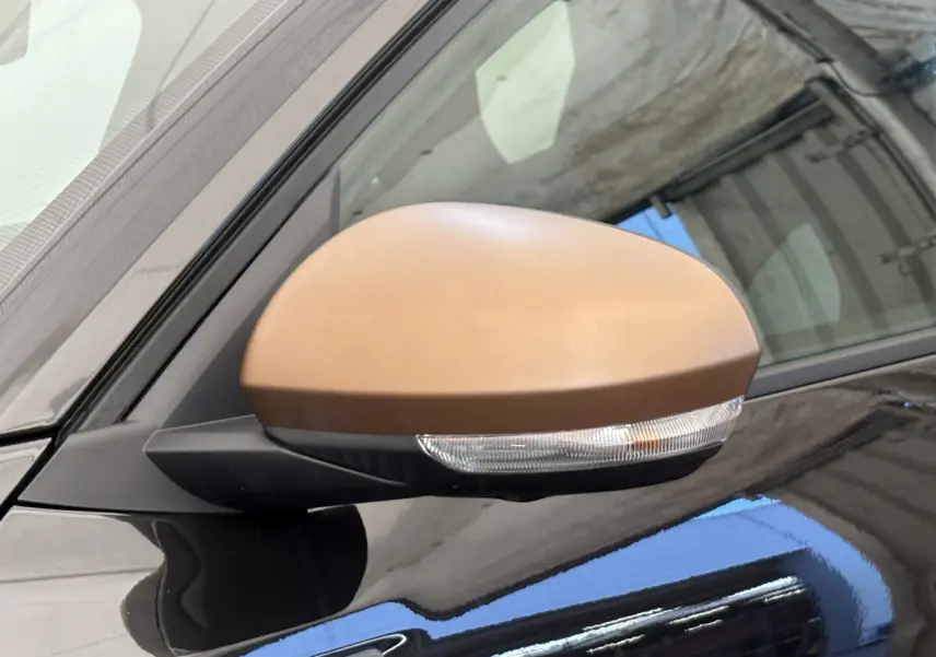 Rétroviseur côté gauche bronze sur Dacia Duster noir 2025, vue rapprochée du miroir avec clignotant intégré.