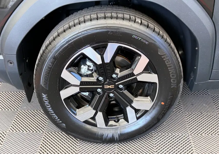 Gros plan sur la roue avant gauche noire du Dacia Duster 2025 avec jante alliage bicolore et logo central.