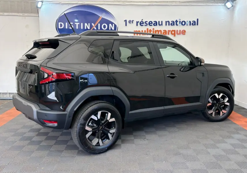 Dacia Duster noir vue de profil côté gauche, avec jantes alliage et barres de toit noires dans un showroom.