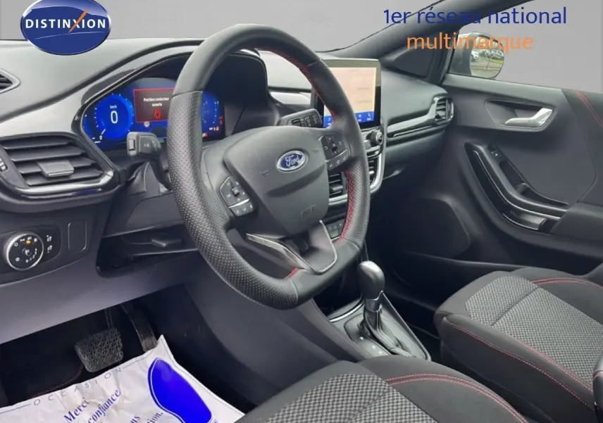 Intérieur du Ford Puma 2024 en vue côté conducteur, volant cuir noir avec surpiqûres rouges et tableau de bord digital.
