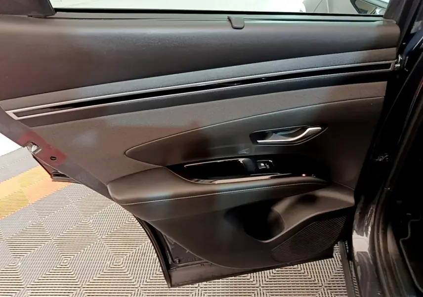 Vue intérieure de la porte arrière droite du Hyundai Tucson gris foncé, avec poignée argentée et commandes de fenêtre.