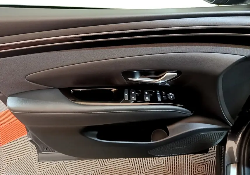 Vue latérale du panneau de porte avant gauche du Hyundai Tucson gris foncé avec commandes électriques et poignée argentée.