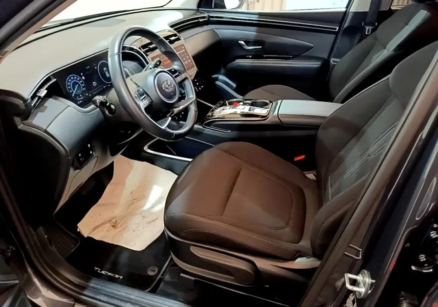 Vue intérieure côté conducteur du Hyundai Tucson 2022, sièges noirs et tableau de bord digital avec écran tactile.
