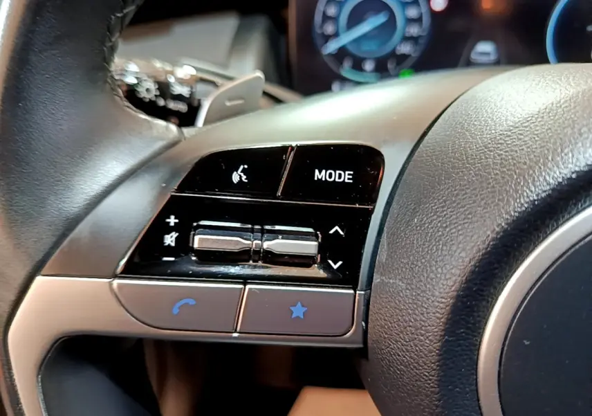Gros plan sur les commandes gauche du volant cuir noir du Hyundai Tucson 2022, avec boutons mode et volume.
