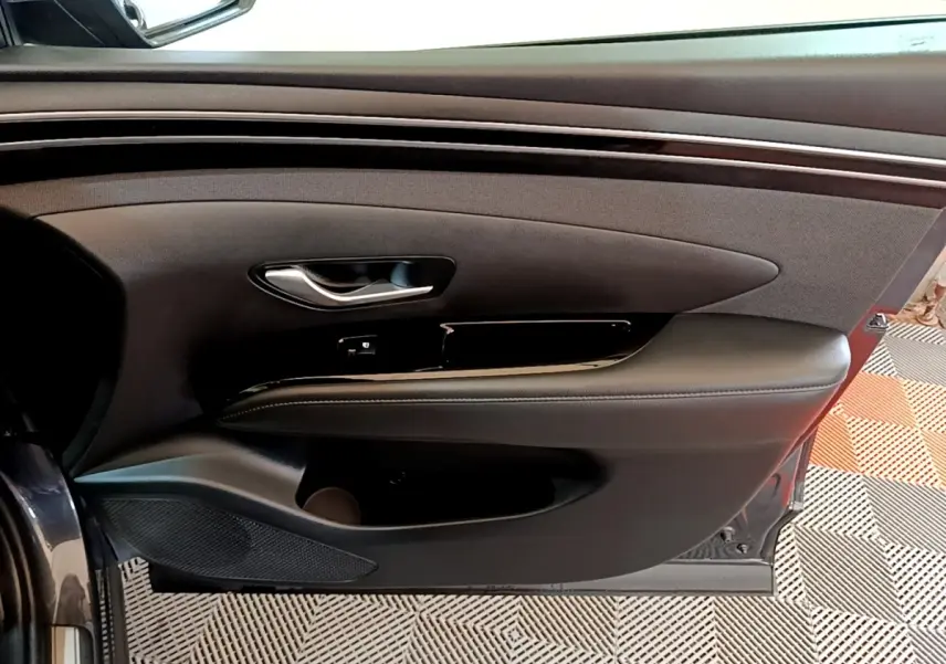 Vue rapprochée de la porte avant gauche du Hyundai Tucson gris foncé, avec garniture noire et poignée argentée.